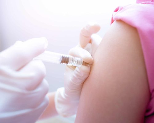 Impfung wird in den Oberarm einer Frau im rosa Shirt verabreicht, medizinische Fachkraft trägt Handschuhe, Bild zeigt Immunisierung in einer Zusammenarbeitspraxis in Buchen.