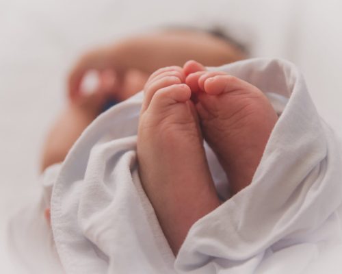 Sanfte Nahaufnahme eines Neugeborenen mit gefalteten Händen, eingewickelt in weißes Tuch, vermittelt Wärme, Geborgenheit und den Beginn eines neuen Lebens. Perfekt für Familien- oder Gesundheitsseiten.
