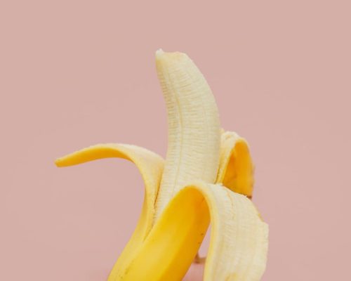 Banane halb geschält auf rosa Hintergrund, frisches Obst mit gelber Schale und cremigem Fruchtfleisch, gesund und lecker.
